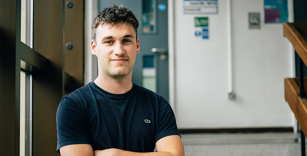 Male student portrait smiling at the camera with their arms crossed in a black top