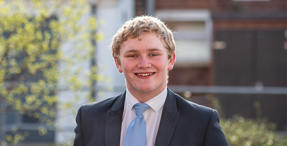 Male Student portrait smiling at the camera wearing a suit with a pale blue tie