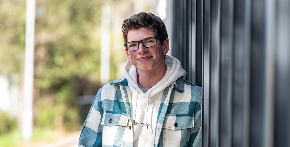 Male Student portrait smiling at the camera wearing a blue and white checked jacket and white hoodie