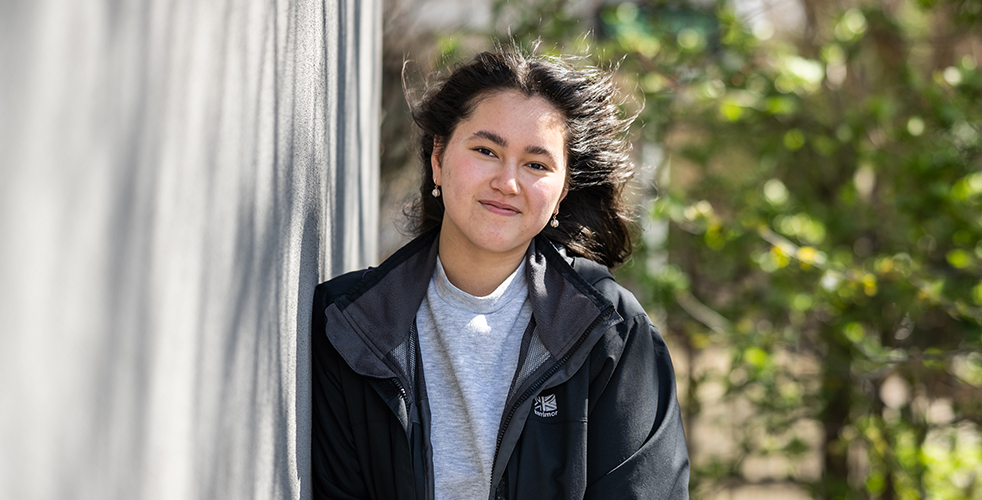 Female Student portrait smiling at the camera wearing a black coat with a grey jumper underneath
