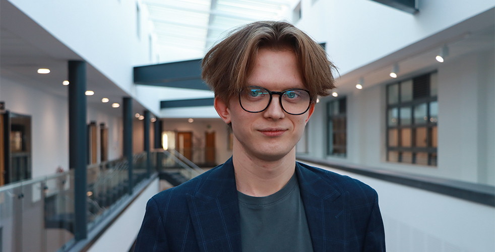 Student smiling at the camera with brunette hair black rimmed glasses in a blue jacket and top