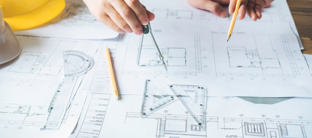 Two hands pointing at an a architects floor plan one hand holding a pencil and one holding a compass
