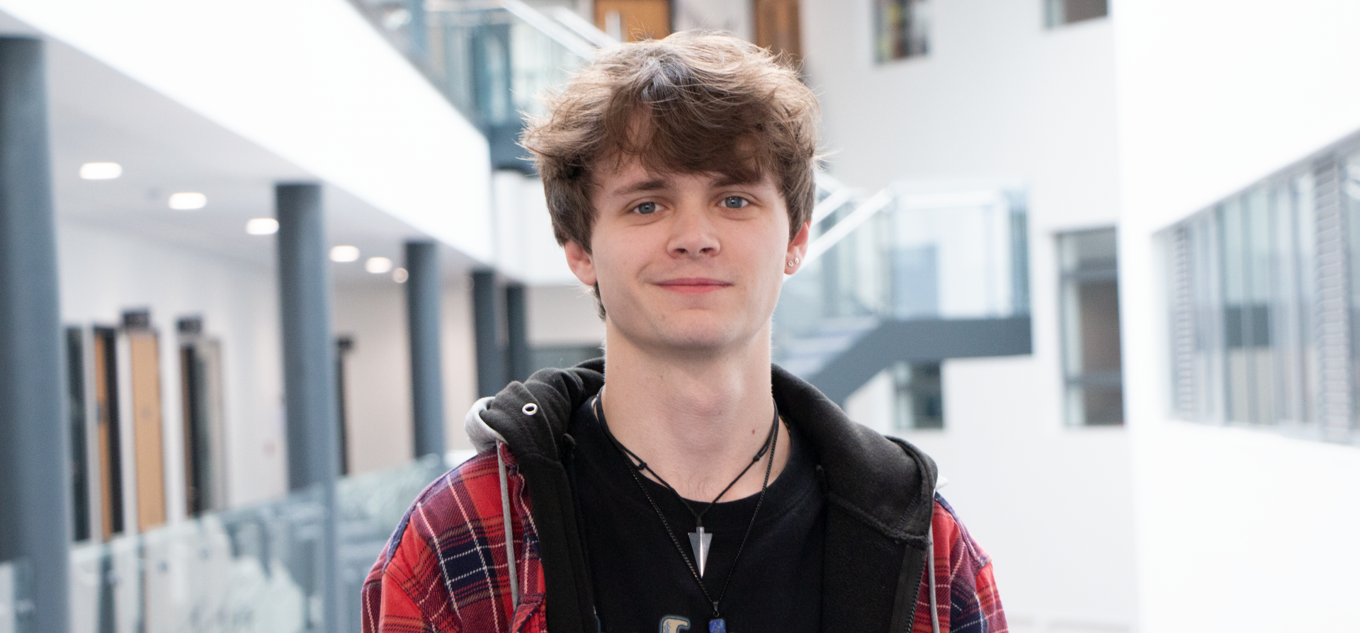 Boy with brunette hair wearing a red checked jacket smiling at the camera