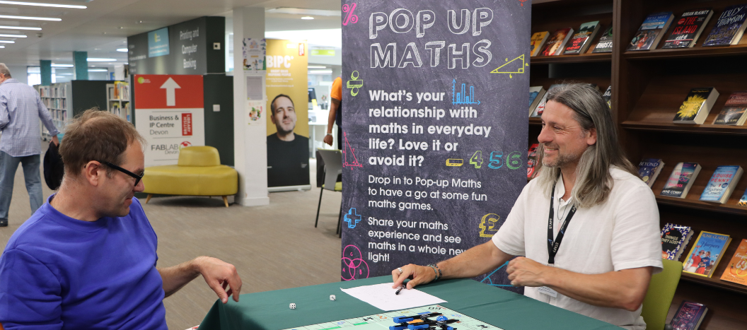 Pop Up maths stand with two people playing monopoly