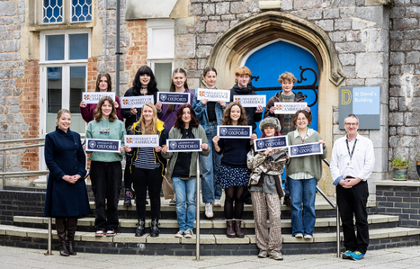 Future Oxbridge students stood on steps outside St David's building holding signs of the university that they have been offered places