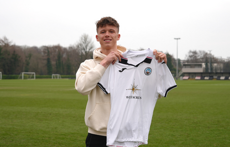 Exeter College Football student holding up a Swansea City AFC Club Football shirt stood on a football pitch