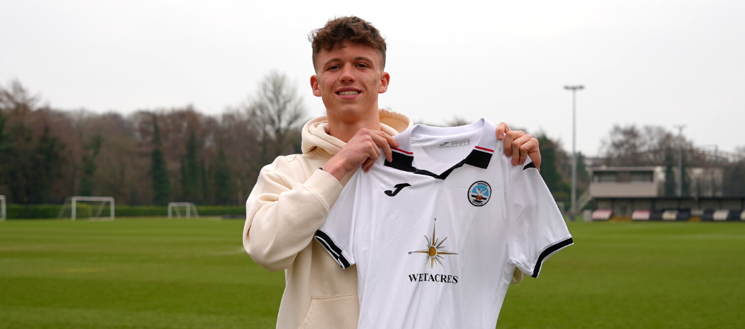 Exeter College Football student holding up a Swansea City AFC Club Football shirt stood on a football pitch