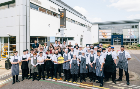 A group of catering students standing in chef whites and black and white aprons in front of the Michael Caines @34 building.