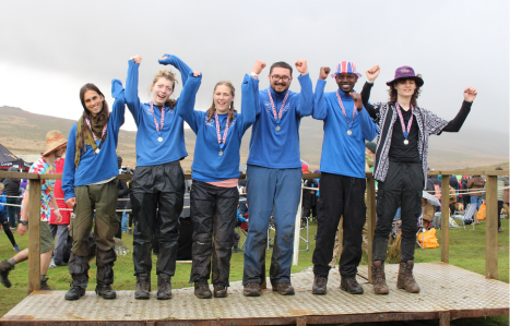 Ten Tors group stood on wooden podium with their arms in the air cheering and their medals on