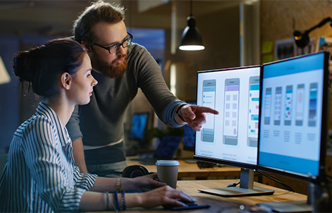 Two people pointing at a computer screen with web design templates of a phone on