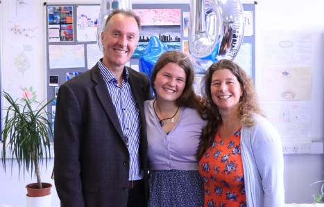 A student poses with her parents and they all smile at the camera.