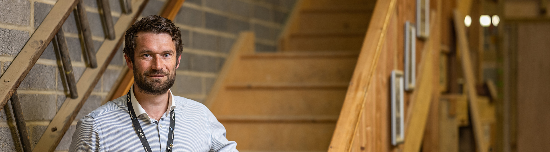 Construction teacher stood at the bottom of some wooden stairs smiling at the camera