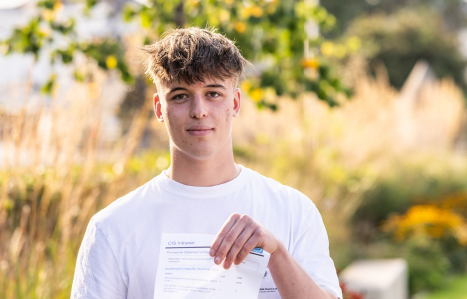 A male student holds his results and smiles at the camera