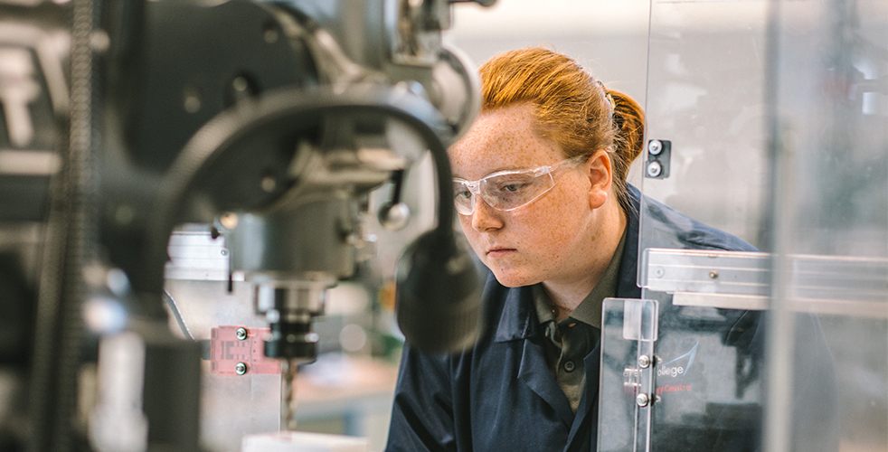 Female Engineering student working on milling machine in workshop wearing safety goggles