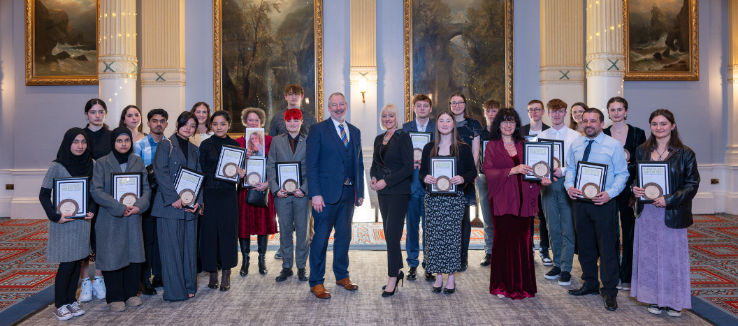 Large group of students stood together holding awards smiling at the camera