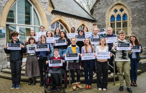 A group of students hold up Oxford and Cambridge signs and smile at the camera