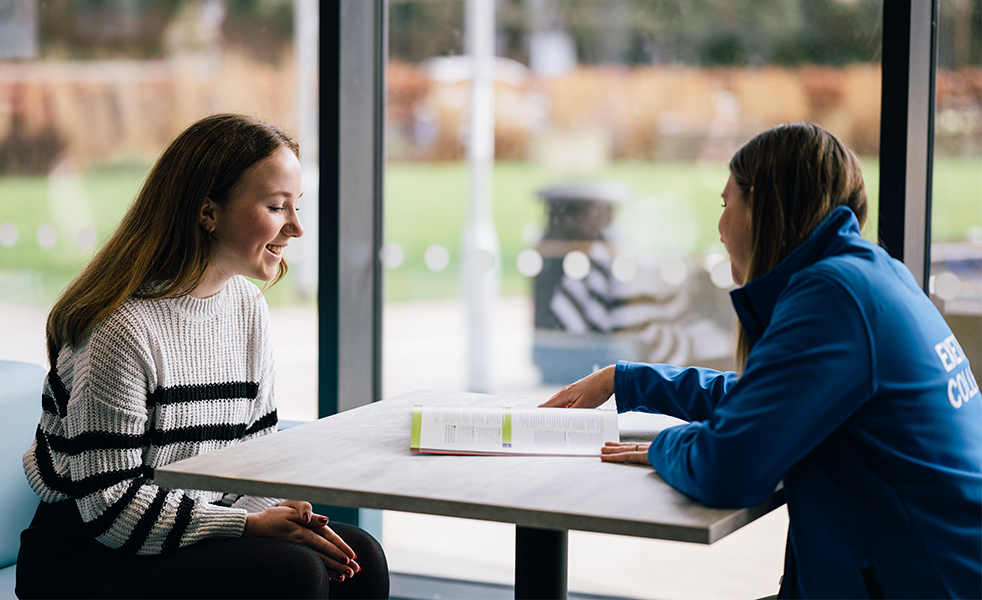 Friendly college Adviser chatting to a student showing pages of course guide