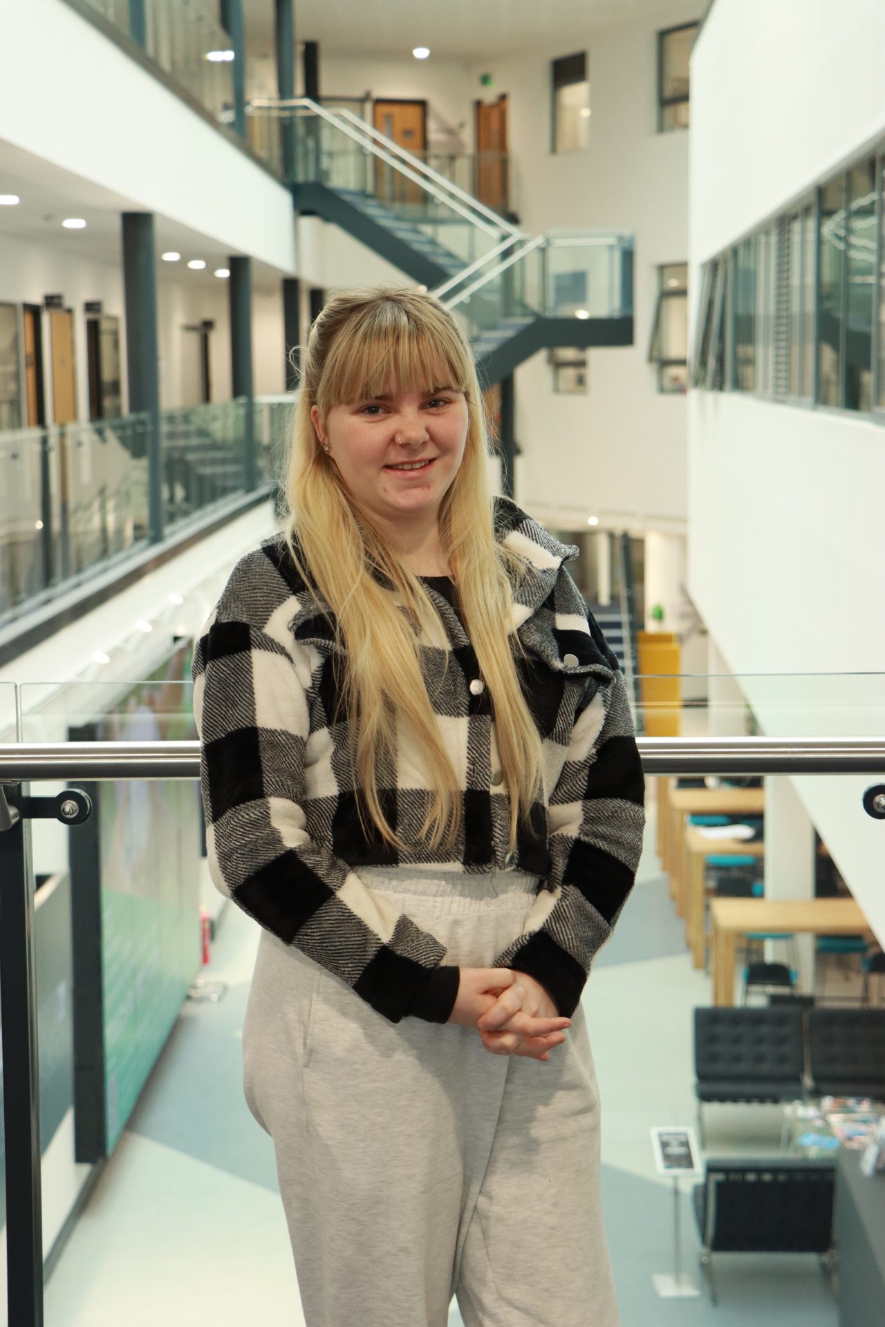 A girl with blonde hair smiles at the camera wearing a black and white chequered shirt.