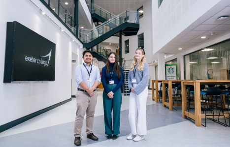 Two female and one male apprentices stand in a line in the foyer of a building.
