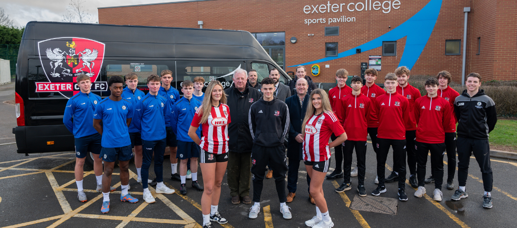 A group of female and male football players stood in front of branded bus outside of the Exeter College sports pavilion