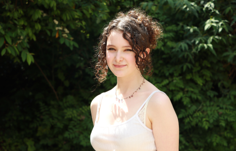A young women smiles at the camera wearing a white strappy top.