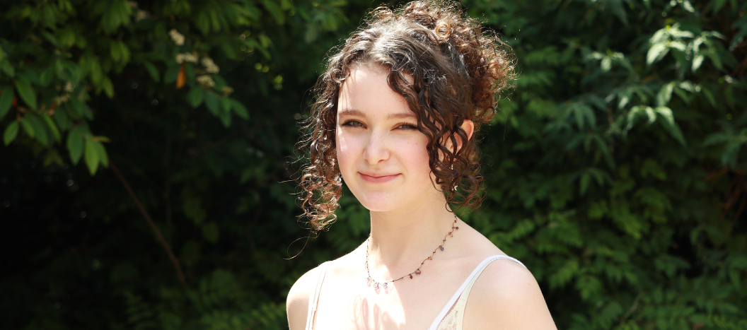 A young women smiles at the camera wearing a white strappy top.