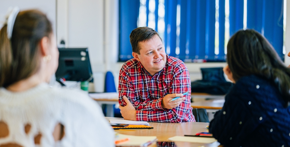 Focus on a male adult learner who is smiling at other learners