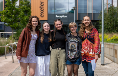 Students collecting their IB results stand in front of the college hugging one another.