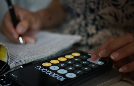 hand on a calculator with a notebook and pen behind