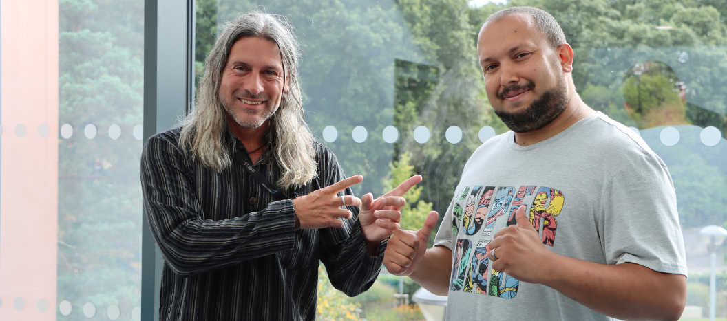 A male adult learner and his tutor smile at the camera with their thumbs up