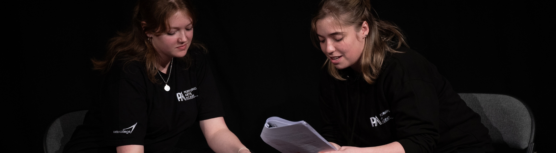 two students sat down looking at scripts together on a dark stage