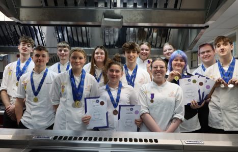 Students in their chef whites post in a kitchen with their competition medals