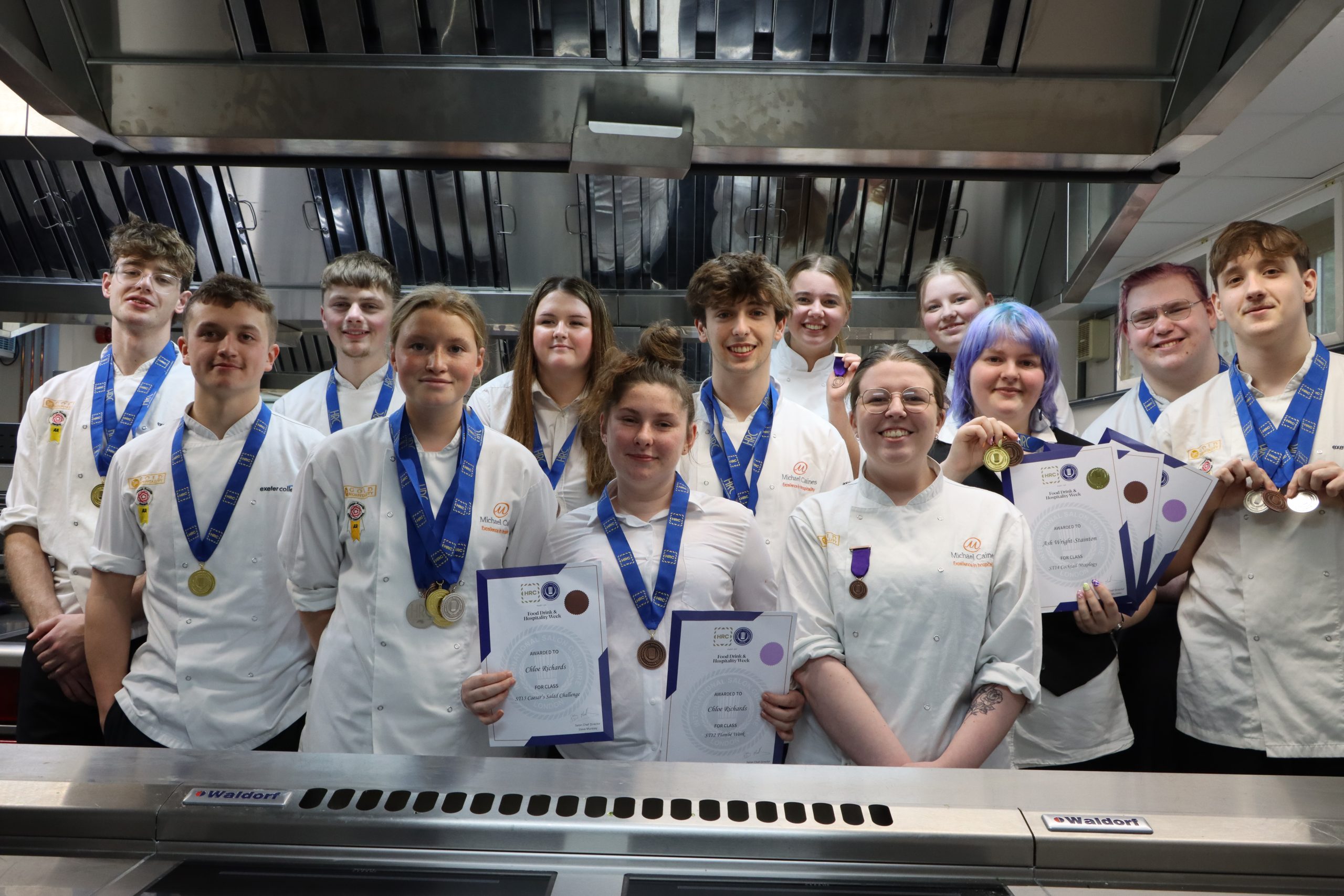 Students in their chef whites post in a kitchen with their competition medals
