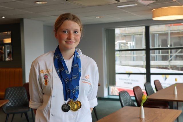 A young female chef stands in her chef whites wearing her medals