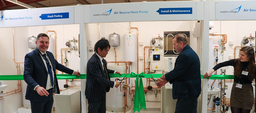 four people holding a green ribbon, two of the people are holding scissors about to cut the ribbon