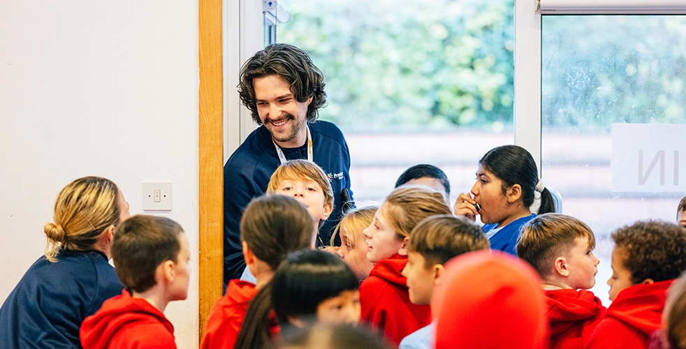 Male teaching student surrounded by children in a sports hall