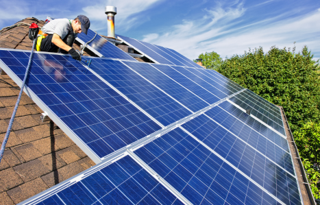A man installs a solar panel on the roof of a house.
