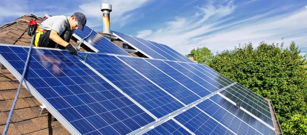 A man installs a solar panel on the roof of a house.