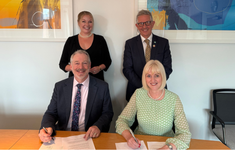 A piece of paper is signed and four people smile at the camera.