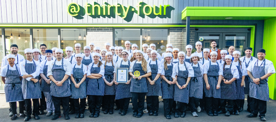 Student chefs line up outside restaurant with trophy and certificate