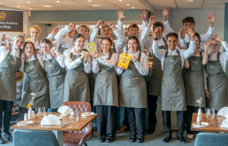 Front of house students hold up an award and raise their arms in celebration