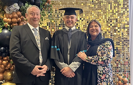 Student in their graduation gown stood in between their parents 
