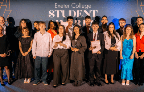 A group of student award winners stand on stage with their trophies.