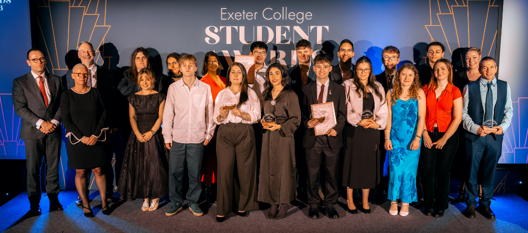 A group of student award winners stand on stage with their trophies.