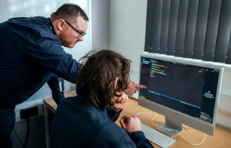 student reviewing code on mac computer with teacher stood beside them pointing at screen
