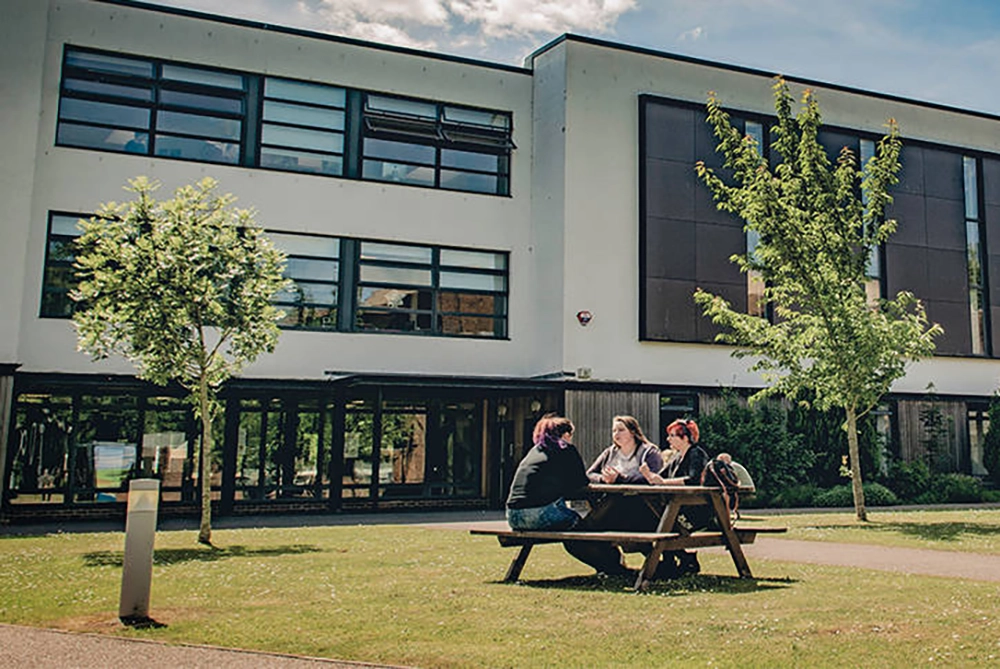 Three students sat on a bench talking