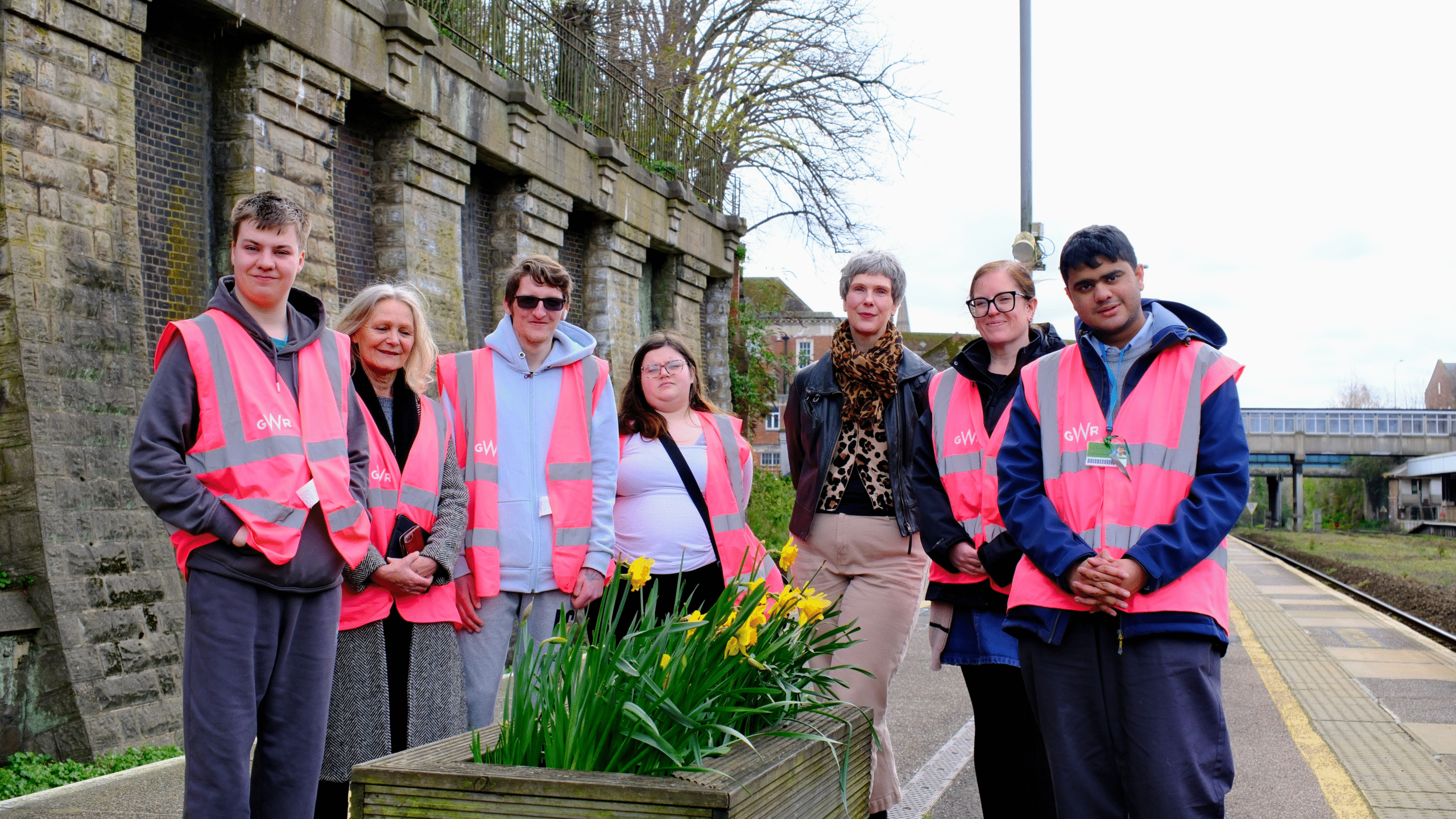 People pose in front of a flower bed at a train station