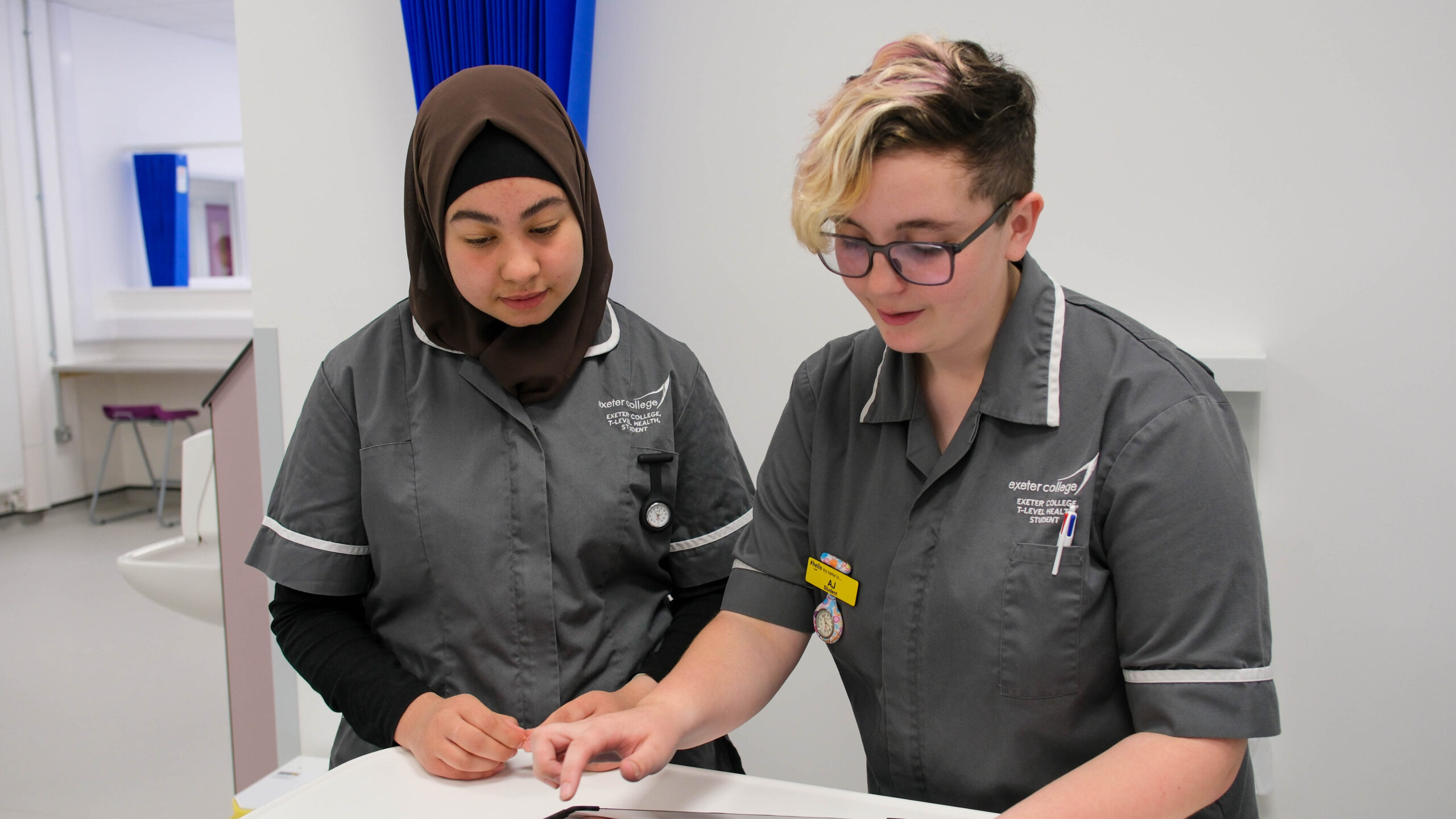 Two students look at a tablet in a hospital training settting. 