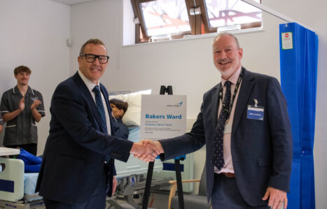 Two people shake hands in front of a plaque at Exeter College's new hospital training ward.