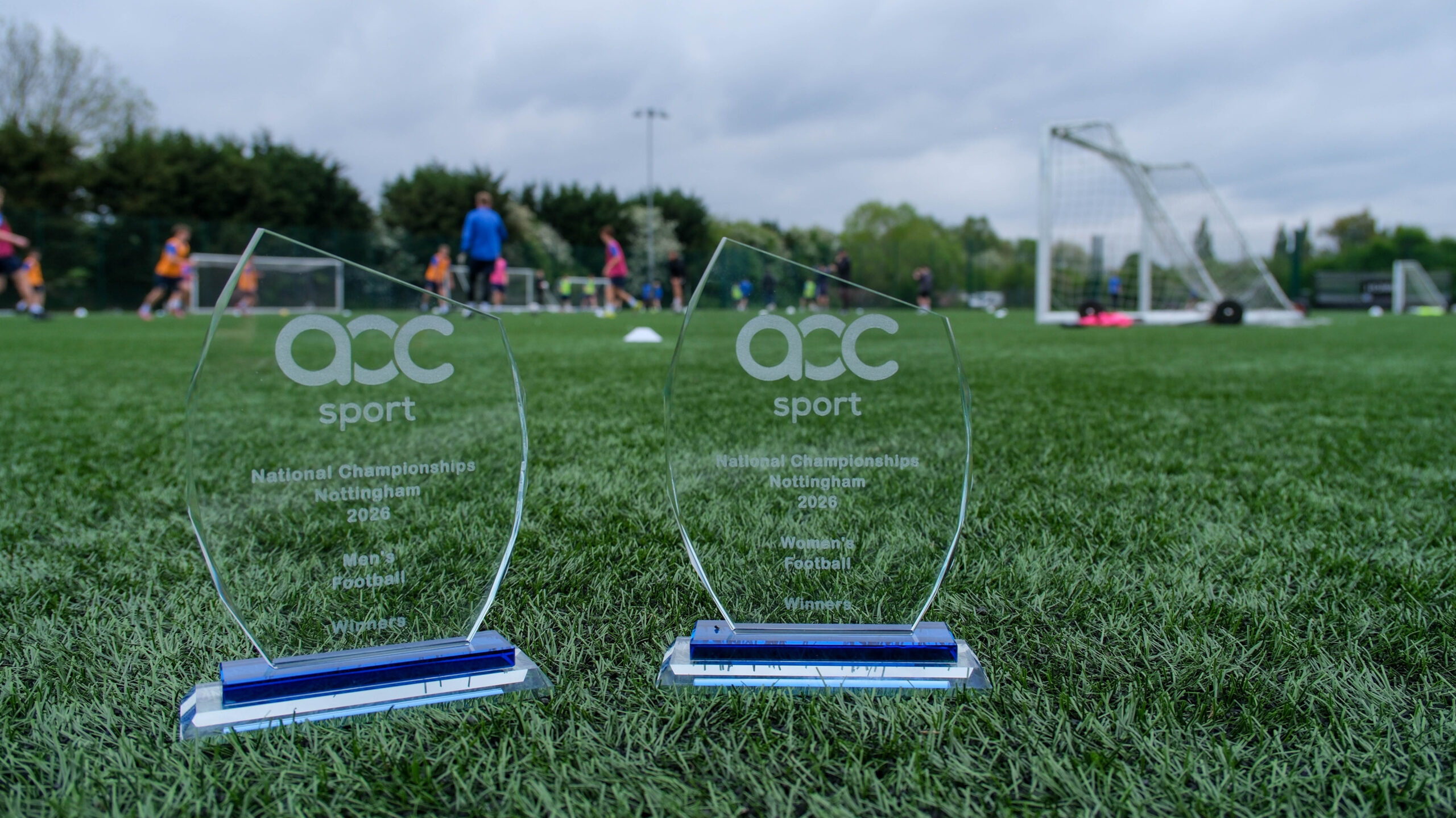 Two AoC trophies on a football pitch at Exeter College